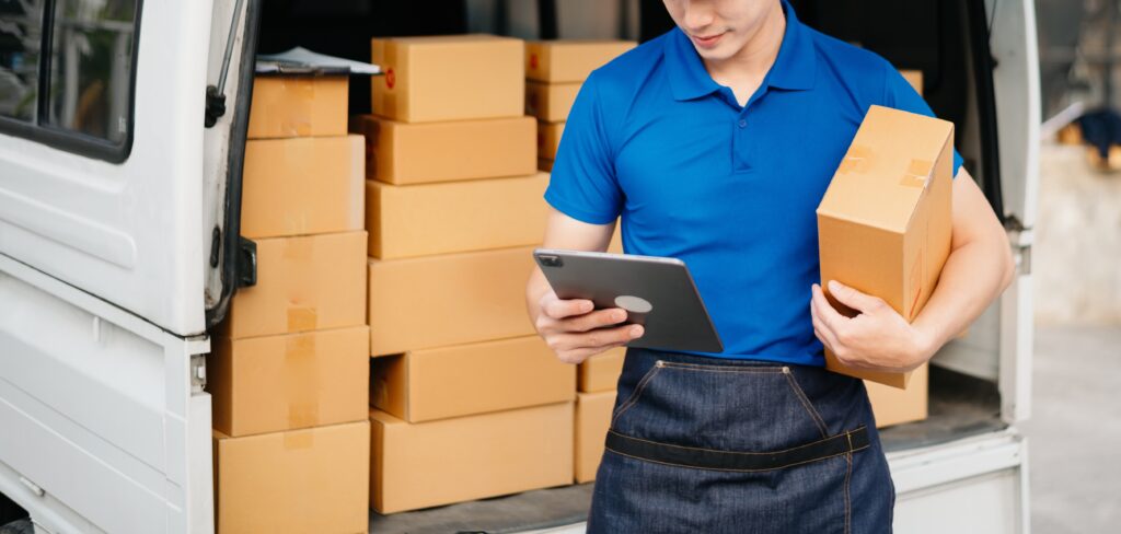 Man outside of his delivery truck holding a tablet with package under his arm getting ready to deliver it to the customer's home