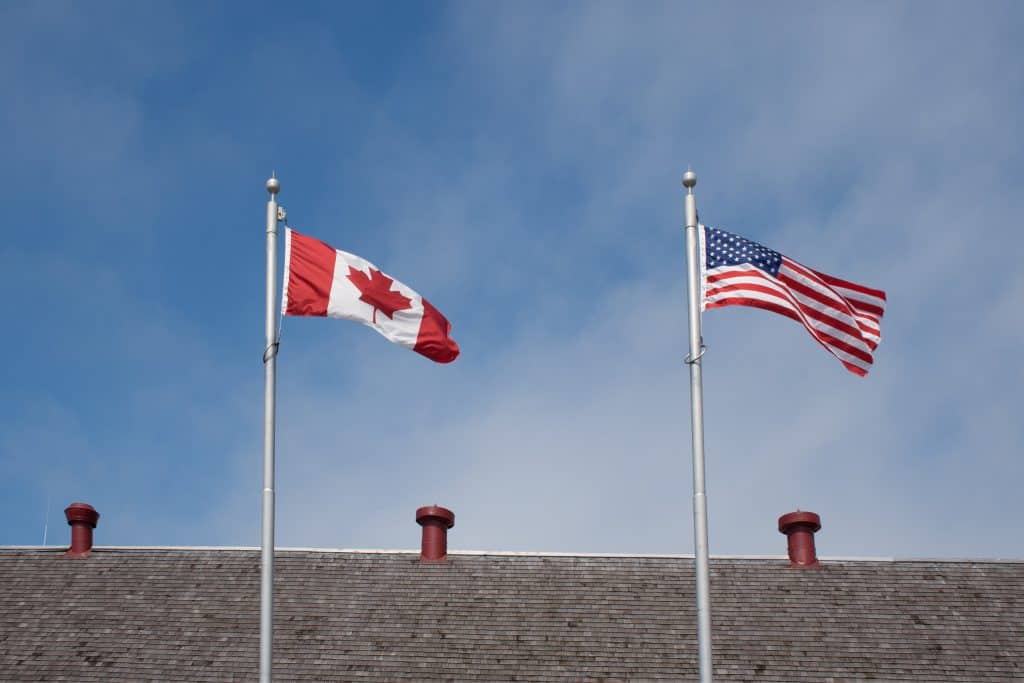 Canadian and U.S. flags flying side by side above a border facility, symbolizing cross-border trade and fulfillment partnerships.