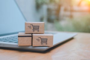 Small ecommerce shipping boxes with shopping cart icons stacked on a laptop, symbolizing online retail and cross-border parcel delivery